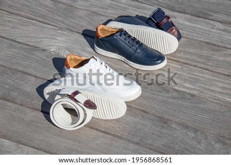 White and navy blue leather sneakers with matching belts on a bench and boardwalk.