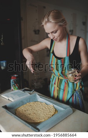 Young blonde woman in color apron cooking pizza at kitchen