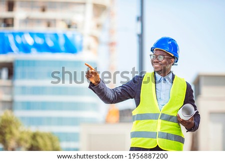 Portrait of smiling engineer in hardhat standing at construction site holding blueprint. Portrait Of happy young Construction Worker On Building Site. Professional engineer in safety equipment 