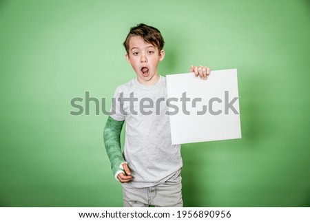 cool school boy with green hand plaster holding white board in front of green background