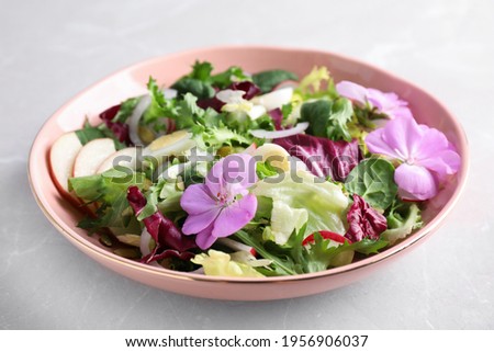 Fresh spring salad with flowers on grey table, closeup