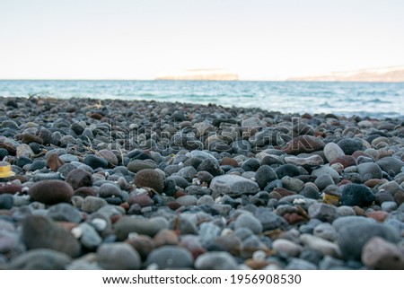 Black pebbles on a black sand beach in Santorini  island, Greece. Sunny day, calm sea