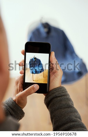 a young caucasian man takes a picture, with his smartphone, of a shirt to sell it on an online marketplace app to sell and buy secondhand goods