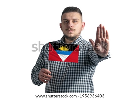 White guy holding a flag of Antigua and Barbuda and with a serious face shows a hand stop sign isolated on a white background.