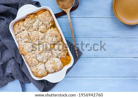 Freshly baked drop biscuit peach cobbler with apron and wooden spoon shot from top view.