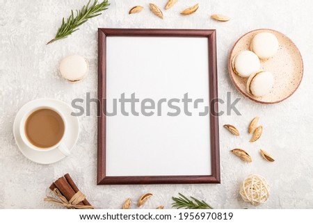 Brown wooden frame mockup with cup of coffee, almonds and macaroons on gray concrete background. Blank, top view, flat lay, still life.