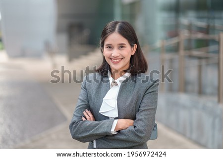 Portrait young attractive Asian business woman wear formal gray suit standing confident with arms crossed outdoor with city background. Cheerful manager secretary job smiling happy looking at camera.