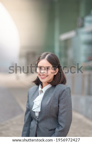 Portrait professional young Asian business woman with formal elegant suit standing confident with beautiful cheerful smile look forward. Person posing outdoor in modern city outside office building.  