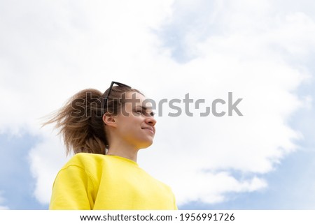 Happy smiling young girl stands outside and looking in the distance on sky background. Joy and gladness concept.
