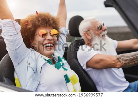 Trendy senior couple having fun inside convertible car - Multiracial mature people on a road trip with cabriolet car Royalty-Free Stock Photo #1956999577
