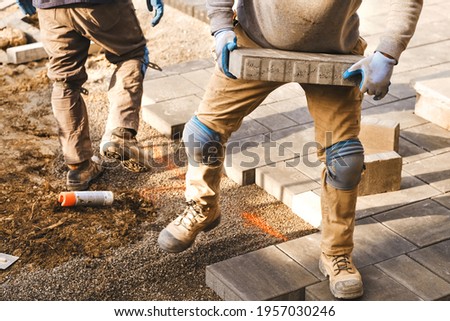 landscaping workers laying paving stones at residential home for quality interlock, garden and home renovation project. Spring is good season to hire contractors for the home improvement around house. Royalty-Free Stock Photo #1957030246