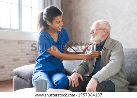 Female attending physician holding stethoscope listening old patient during homecare visit. Doctor checking heartbeat examining elder retired man at home. Seniors heart diseases, cardiology concept. Royalty-Free Stock Photo #1957064137