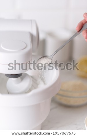 Add sugar with a spoon to a working mixer.Sugar being pouring into bowl.Close-up