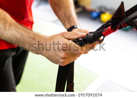 Hands of handsome young man training in gym with TRX Fitness