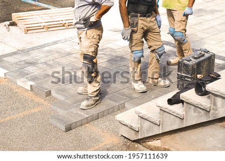 Three construction workers working on landscaping construction site, laying paving driveway stones slabs for quality garden patio stonework, home renovation project. Prospective view of man onsite job Royalty-Free Stock Photo #1957111639