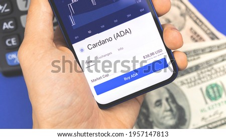 Man is using smartphone for buying Cardano ADA crypto currency, mobile trade and stock exchanges concept background Royalty-Free Stock Photo #1957147813