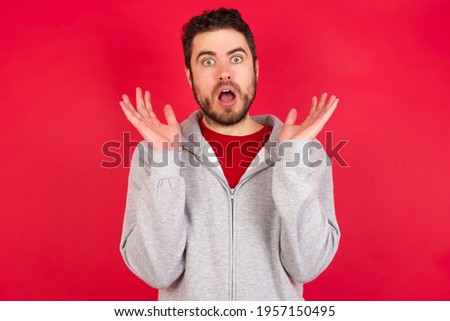Surprised terrified Young caucasian man wearing tracksuit over red background Gestures with uncertainty, stares at camera, puzzled as doesn't know answer on tricky question, People, body language,