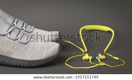 Light gray sneakers and bright yellow headphones on a dark gray background. Sports lifestyle. Colors 2021.