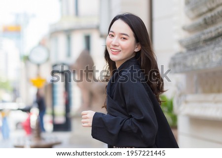 A picture of a beautiful long haired Asian beautiful woman in a black robe smiling happily 
walking and looking out in the city outdoors.