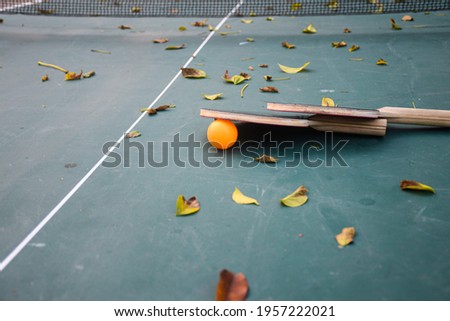 A picture of a table tennis table in a deserted stadium full of fallen leaves due to the lack of people playing during the COVID-19 epidemic.