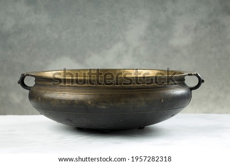 Urule or Brass vessel,an empty traditional  south Indian cooking vessel which is an antique piece placed on grey textured background. Royalty-Free Stock Photo #1957282318