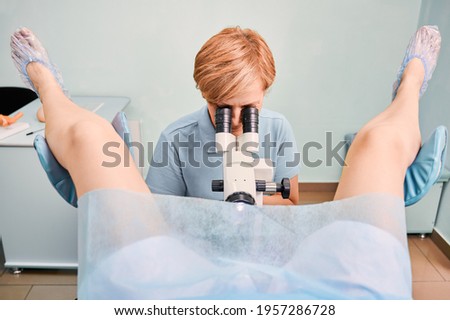 Front view of doctor in blue shirt examining woman with colposcope in gynecological clinic. Female patient laying in gynecological chair while gynecologist doing colposcopy examination. Royalty-Free Stock Photo #1957286728