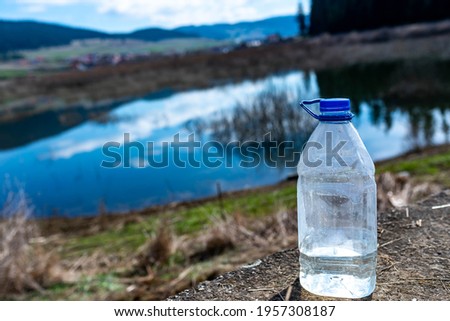 Forgotten plastic bottle near a clean small lake, conceptual image of human negligence.