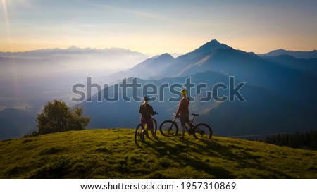 Two females on mountain bikes talking and looking at beautiful sunset Royalty-Free Stock Photo #1957310869