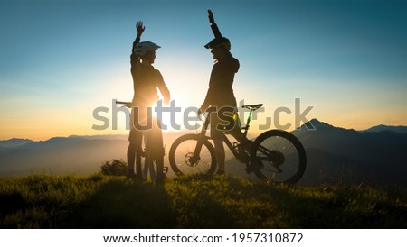 Two happy woman high five over the sunset after a successful mountain biking trip in the mountains. Celebrate a cross country cycling journey. Royalty-Free Stock Photo #1957310872