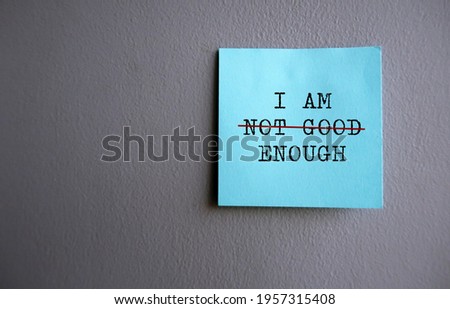 Blue note on gray wall with text I AM NOT GOOD ENOUGH with red crossing on NOT GOOD , concept of self worth , stop striving for approval, more valid , more loved or validation , you are good enough Royalty-Free Stock Photo #1957315408