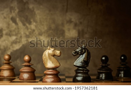 Wooden knights chess pieces facing each other on a vintage chessboard with pawns in the background. Rivalry concept, textured background. Royalty-Free Stock Photo #1957362181