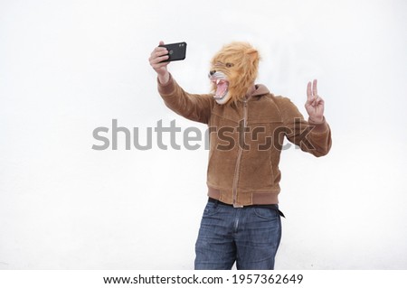 A man with a roaring lion full mask taking a selfie with his phone isolated on white background