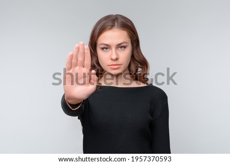 Stop sign, palm on camera, symbol - donT move. Serious young brunette woman shows her palm right on camera. Studio shot, gray background