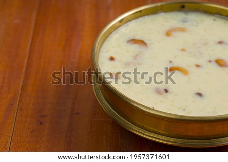 Indian sweet dish Rice Palada  Payasam or Kheer_ main sweet dish made during special occassions_using rice pastha bits,milk,sugar and dry nuts arranged in a brass vessel with wooden background