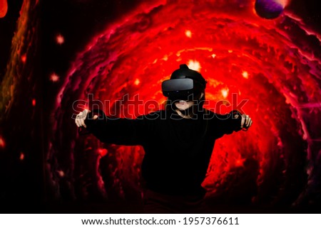 A young girl plays a game in virtual reality glasses holding gamepads in her hands. Bright red background in the playroom. High quality photo