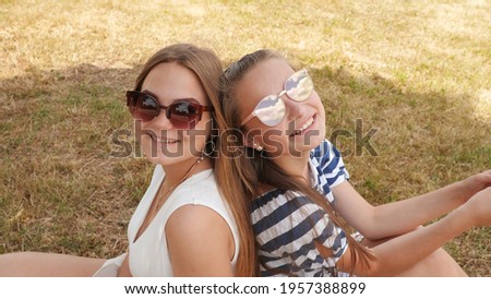 Cheerful female friends in sunglasses are sitting on the grass in the city.