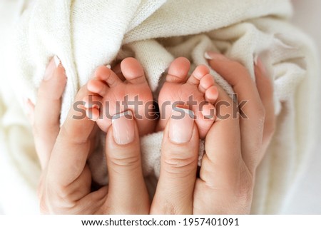 Feet of the newborn in the hands of the mother. Mother holds baby's feet in her hands. Happy family concept.