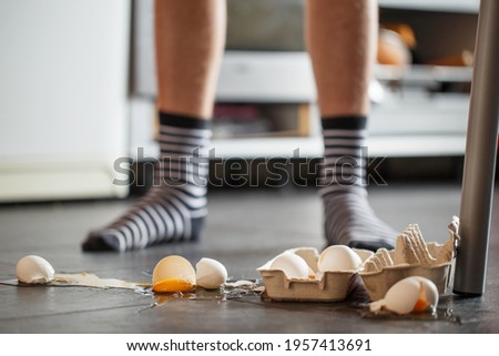 Broken eggs - accident at kitchen, mess. Legs on  background  Royalty-Free Stock Photo #1957413691