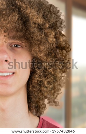 split in half cropped portrait of a young curly European man with long curly hair and a dreamy smile close-up against the window. very lush male hair. curling hair men's. a lock of passion.