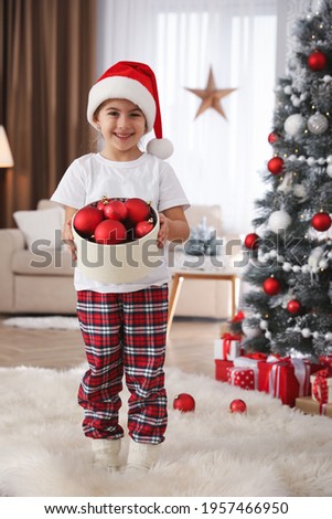 Cute little girl holding box with Christmas balls at home