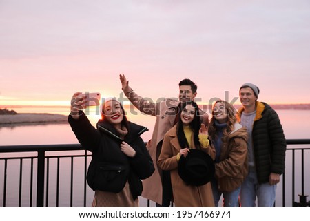 Group of friends making selfie near river at sunset