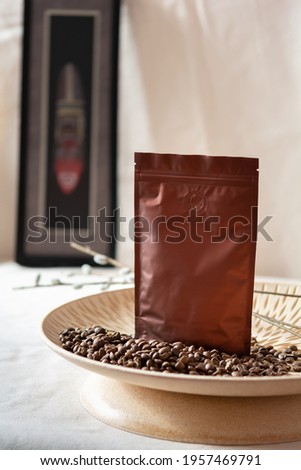 Blank coffee packaging, coffee seeds in wooden decorative plate, decorative african mask on background and willow branches, coffee packaging mockup with empty space to display your branding design.