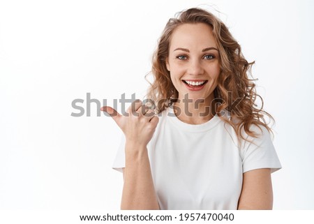 Image of stylish blond woman points left, shows promotional text aside, smiles and looks satisfied at camera, white background.