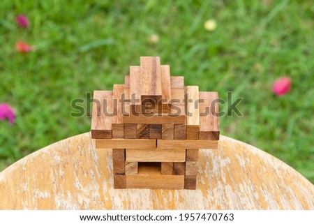 ็House made by wooden block game pieces in the garden with blurred tree at the back, under concept of basic human need "housing" with empty copy space for text quote or background usage