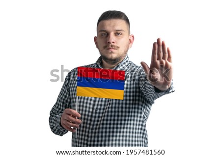 White guy holding a flag of Armenia and with a serious face shows a hand stop sign isolated on a white background.