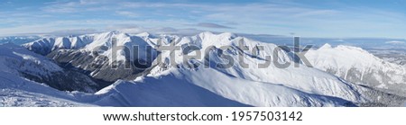 Magnificent panoramic shot of mountain peaks covered in snow during the winter season. A blue sky with few white clouds can be seen in the background. Zakopane - Kasprowy Wierch