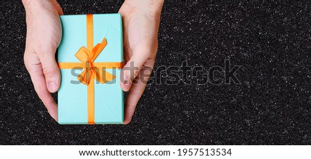hands hold a box of blue with an orange bow against the black wall. View from above. High quality photo
