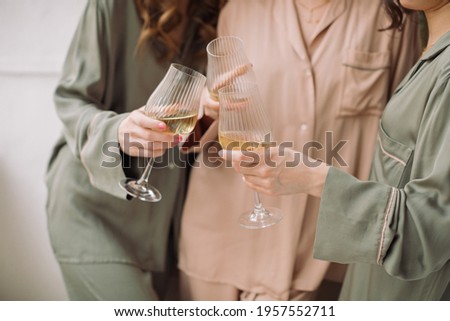 Close up of three friends in silk pastel color pajamas holding glasses of champagne. Girls Pajama Party concept.