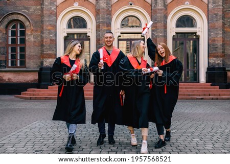 Photo for memory. A group of happy friends of students take a selfie with a graduation document. in robes against the background of the university building.