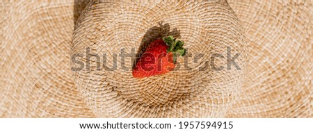 Horizontal banner header of ripe strawberry on a straw hat on the sand.